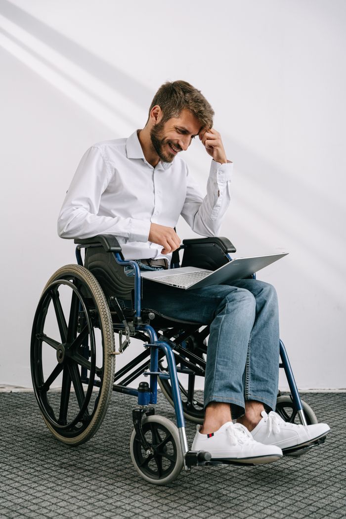Man in wheelchair working on a laptop indoors, showcasing accessibility and technology.