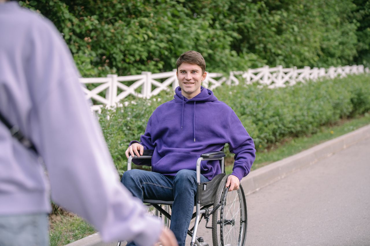 Portrait of a man in a wheelchair wearing a purple hoodie, smiling outdoors.
